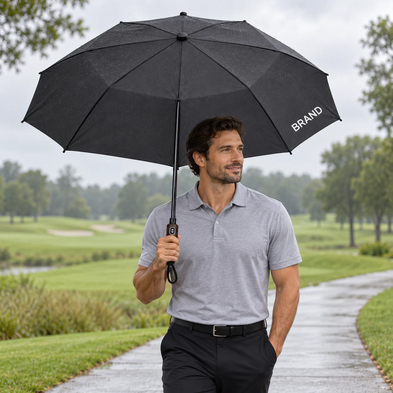 Adult holding a black personalized golf umbrella beside a golf-course walkway