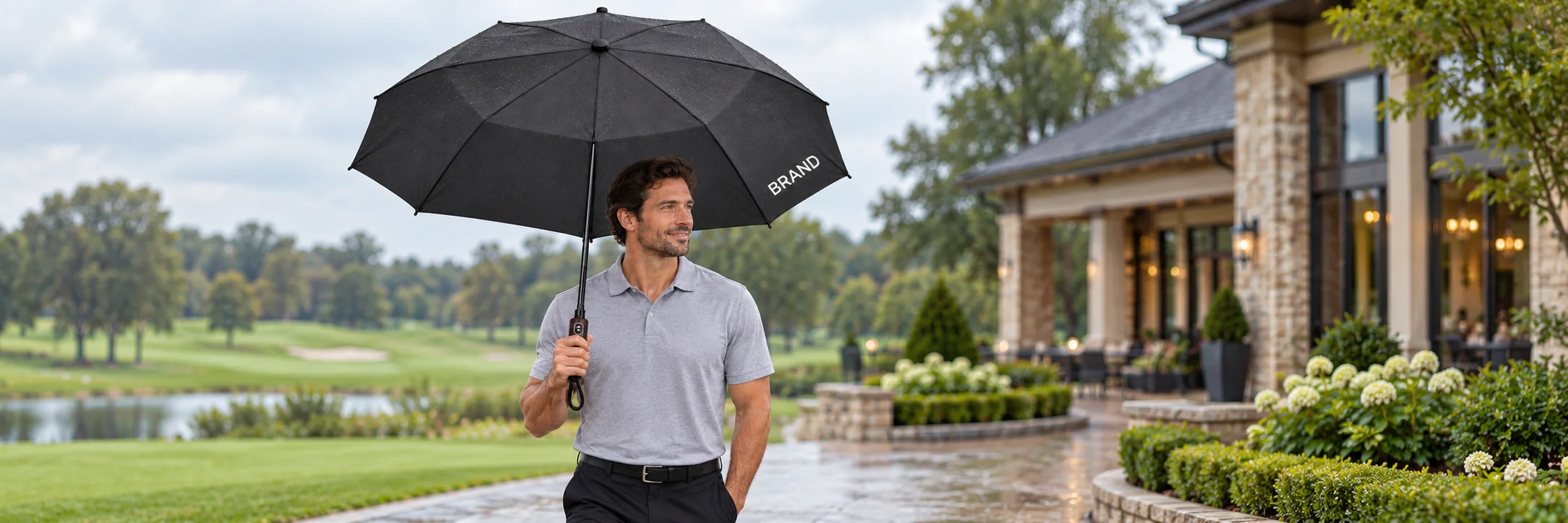 Event participant holding a black personalized umbrella near a golf-course clubhouse
