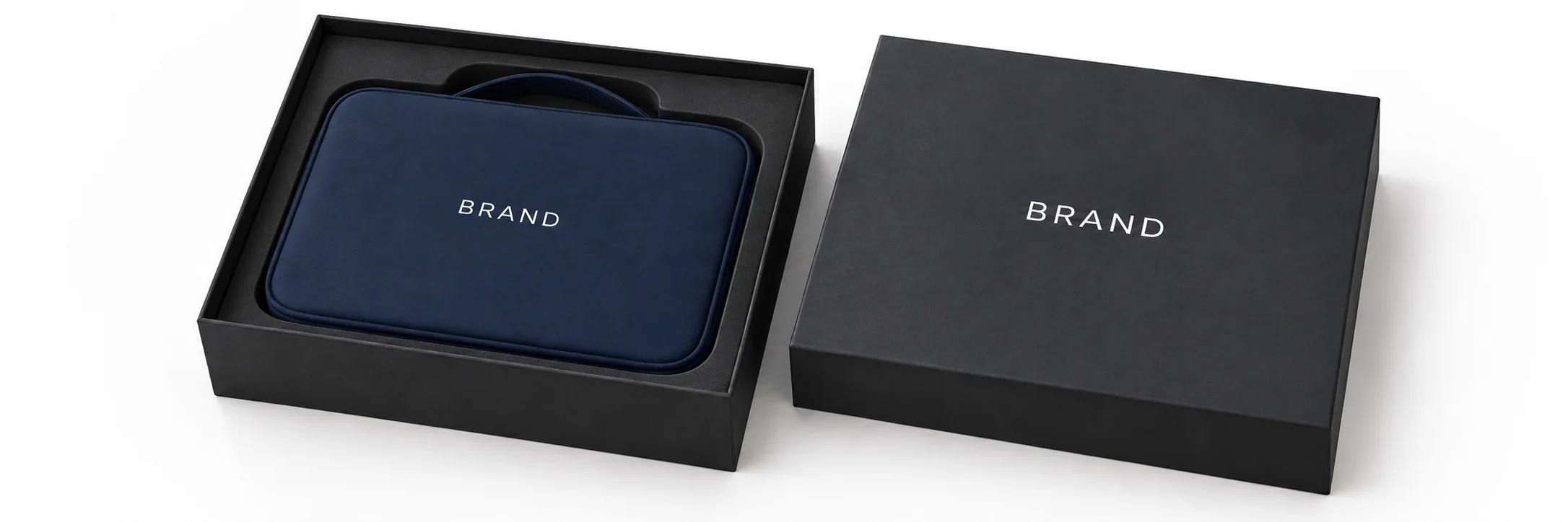Closed navy toiletry organizer with white lettering inside a fitted charcoal presentation box beside its lid.
