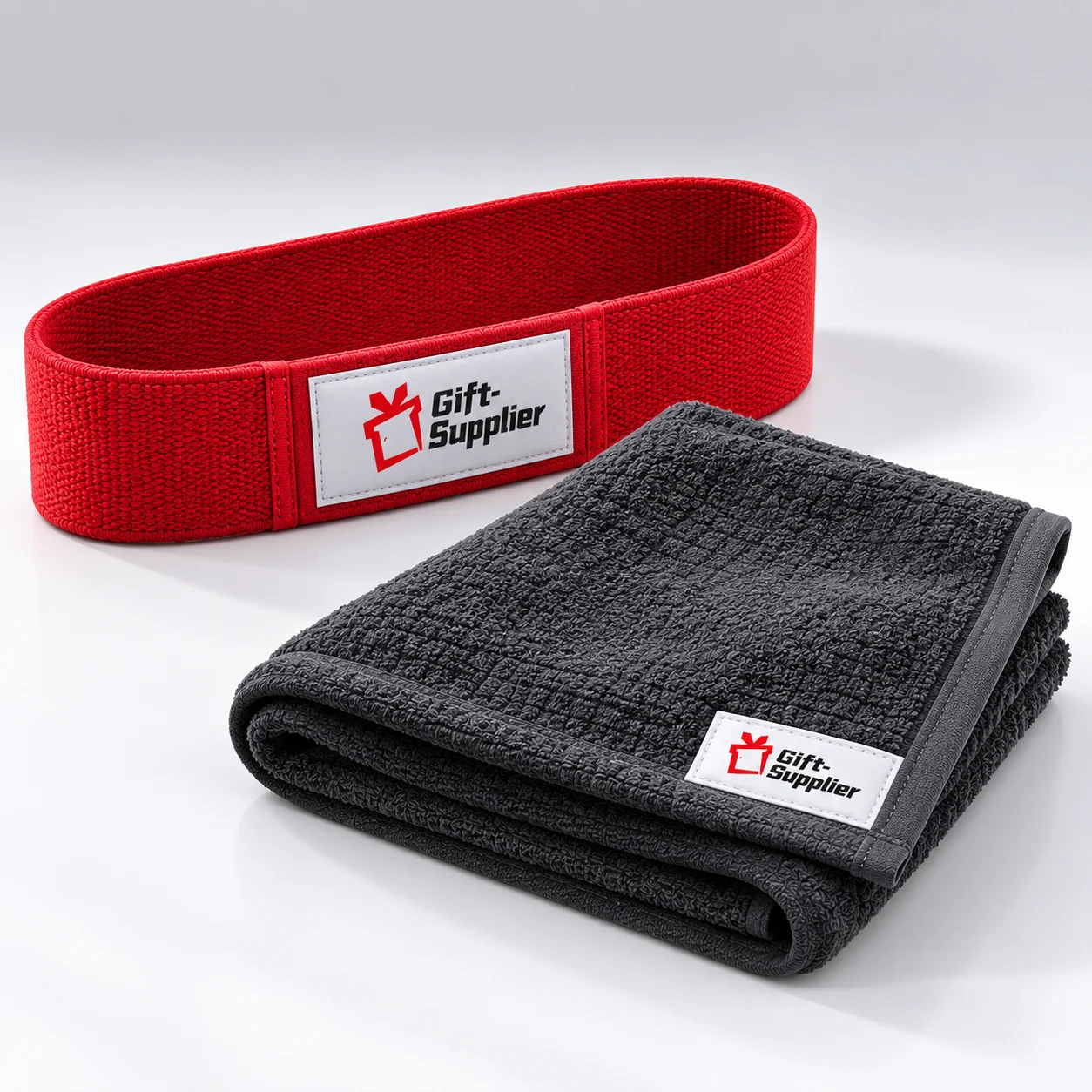 Deep-red resistance loop band and charcoal workout towel with Gift Supplier labels.